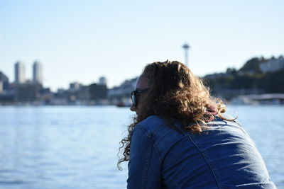 Rear view of woman against river in city against clear sky