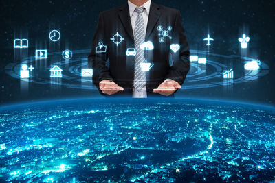 Digital composite image of businessman with symbols over illuminated city
