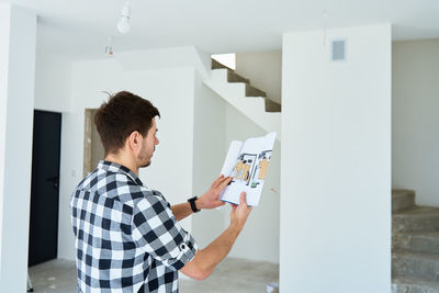 Rear view of woman using digital tablet while standing by window
