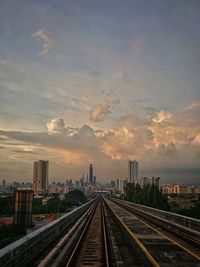 Railroad tracks by buildings against sky during sunset