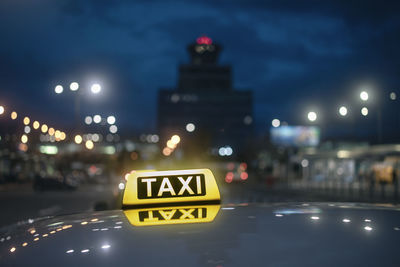 Taxi sign. reflection in roof of car against airport terminal building at night.