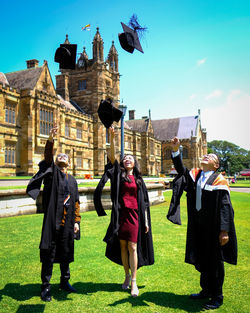 Full length of students wearing graduation gown throwing mortarboard on field during sunny day