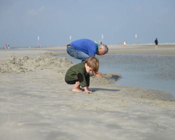 Grandfather with grandson enjoying at beach against sky during sunny day