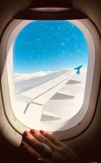 Midsection of airplane wing against sky seen through glass window