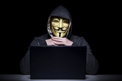 Man in mask with laptop against black background