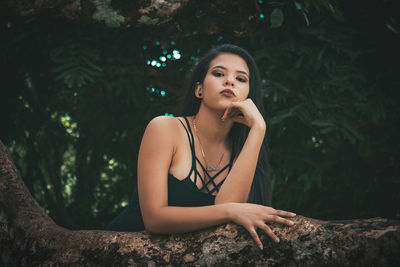 Portrait of young woman looking away while sitting on tree