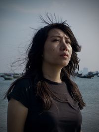 Thoughtful woman standing at beach against sky