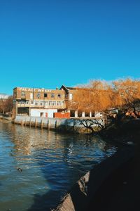 Buildings by river against clear blue sky