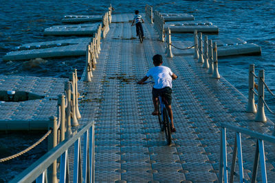 Rear view of men walking on railing by sea