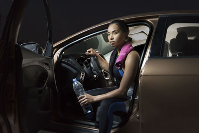 Beautiful woman holding bottle while sitting in car at night