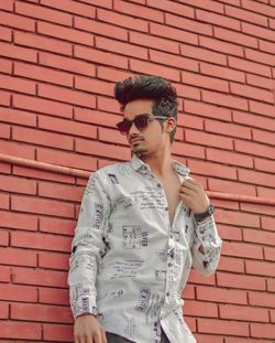 Young man wearing sunglasses standing against brick wall
