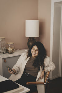 Smiling businesswoman holding smart phone while sitting on chair at office