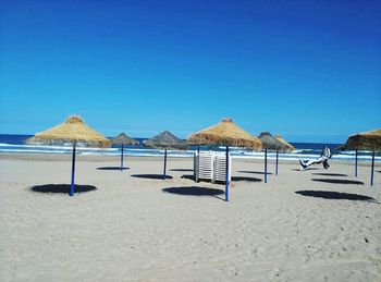 Deck chairs on beach against clear blue sky