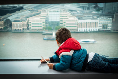 Boy looking at lake through glass while lying on window sill