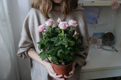 Medium plan of a young woman holding a potted pink rose bush