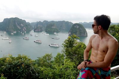 Shirtless man looking at ha long bay while sitting on railing