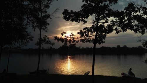 Silhouette trees by lake against sky during sunset