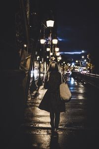 Rear view of woman walking on illuminated street at night