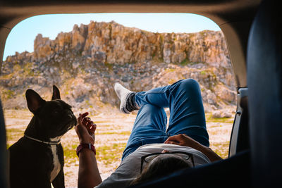 Midsection of man with french bulldog dog sitting on car trunk against mountain