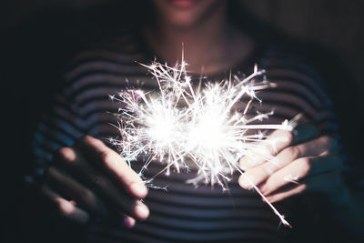 Midsection of person holding illuminated sparklers