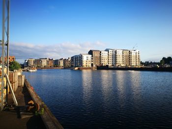 Buildings by river against clear blue sky