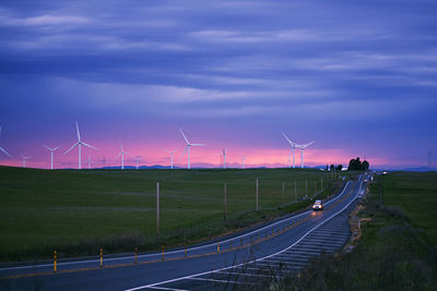 Road passing through field against cloudy sky