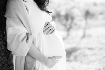 Midsection of pregnant woman with hands on stomach standing against defocused background