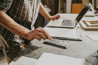 Midsection of male carpenter using calculator on workbench at repair shop