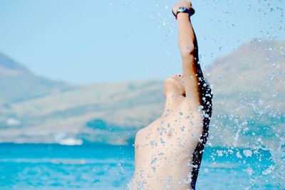 Shirtless man with hand raised in river against sky