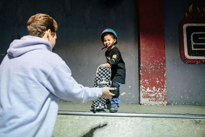 Little boy preps his skateboard to go down a ramp with instructor