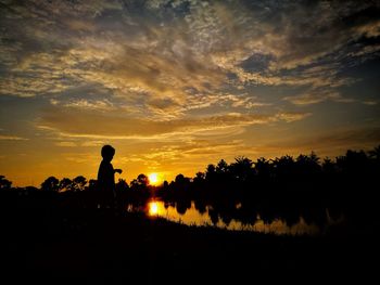 Silhouette man standing on field against sky during sunset