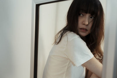 Portrait of beautiful young woman standing against window at home