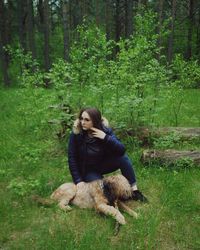 Young woman resting dog on grassy field in forest