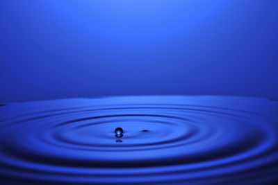 Close-up of drop falling on water against blue background