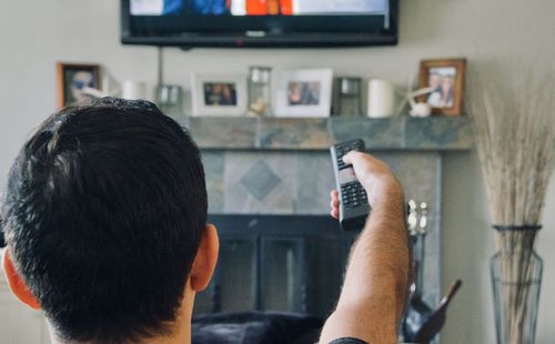 Rear view of man holding camera at home