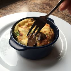 Cropped image of hand holding fork on fresh food in serving dish on table