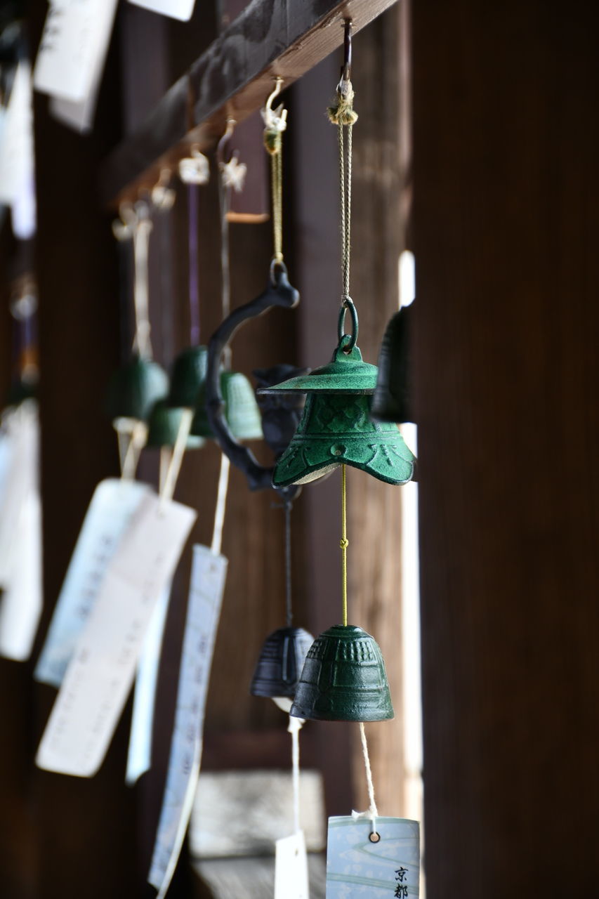 hanging, no people, focus on foreground, metal, indoors, bell, close-up, wood - material, selective focus, built structure, architecture, day, string, religion, belief, group of objects, lighting equipment, spirituality, green color