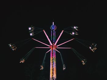 Low angle view of people enjoying illuminated chain swing ride against sky at night