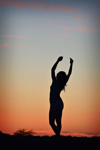Silhouette woman standing with arms raised on field against sky