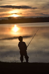 Silhouette man fishing on shore against sunset sky