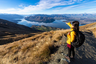 Rear view of woman standing on rock against mountain and sky