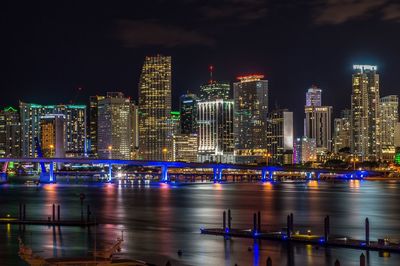 Illuminated buildings by river against sky at night