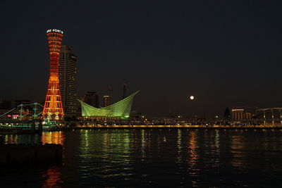 Illuminated buildings by river against sky at night