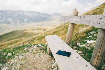 Close-up of mobile phone on wooden bench against mountain