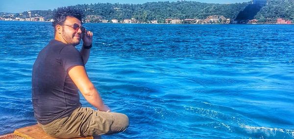 Side view of young man sitting by sea