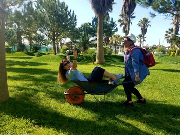 Woman enjoying while sitting in wheelbarrow pulled by friend