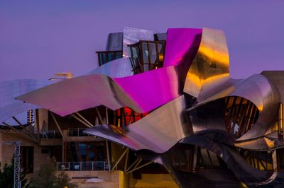 Close-up of sculpture against illuminated buildings in city at sunset