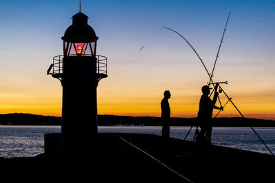 Silhouette people standing by sea against sky during sunset