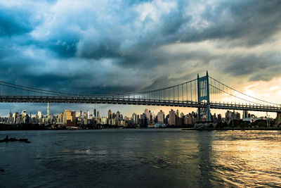 View of suspension bridge over river against cloudy sky