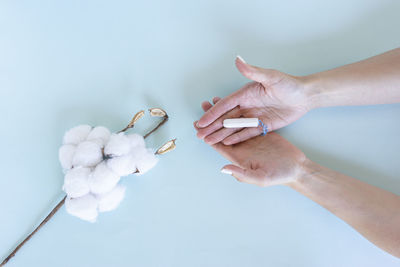 Womans hand holds a sanitary tampon with the cotton lying next to it